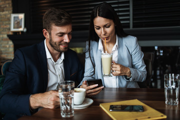 Happy couple man and woman sitting in modern cafe bar or restaurant and drinking coffee.