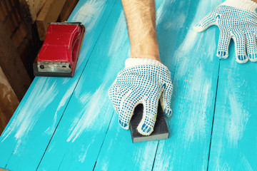 Sanding blue wooden background hand with abrasives in a glove close up - obrazy, fototapety, plakaty
