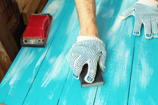 Sanding blue wooden background hand with abrasives in a glove close up