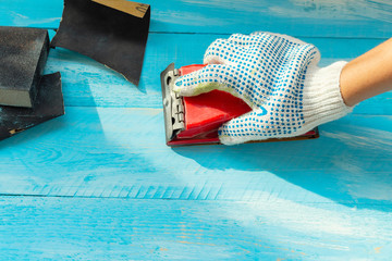 Sanding blue wooden background hand with abrasives in a glove close up