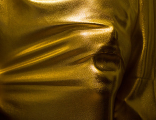 human face pressing through golden fabric