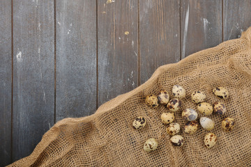 Quail eggs located on burlap on wooden dyed background. Top view.