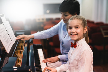 little girl practicing playing piano with her professor assistance