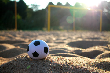 Fototapeta na wymiar soccer ball on the left in the evening sunlight close-up, with goal on the background and sunbeams
