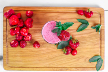 Glass of pink strawberry milkshake or cocktail with strawberries on wood background. Top view