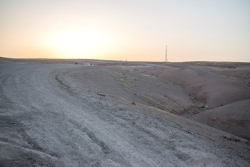 View of a man riding a motorcycle on a dirt road in the Sahara desert in Morocco, Africa. The sun sets behind the mountains.