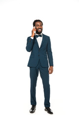 happy african american bridegroom talking on smartphone and standing isolated on white