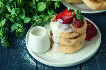 Close up. Traditional rustic breakfast. Freshly made cheese pancakes, poured with cream and decorated with strawberries. Copy space.