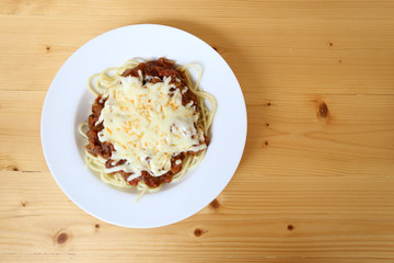 Spaghetti with tomato sauce and a lot of cheese on top, wood table