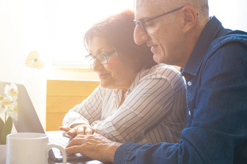 A middle aged couples enjoy the laptop by shopping online and reading news