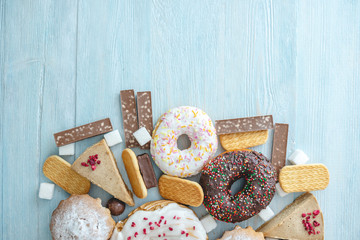 Harmful sweet foods on blue wooden background. Donuts and muffins on the table pile. Unhealthy diet and overweight