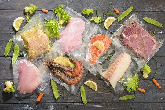 Sous Vide cooking concept. Vacuum packed ingredients arranged on wooden dyed background. Top View.