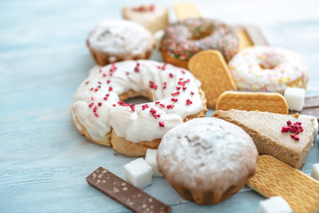 Harmful sweet foods on blue wooden background. Donuts and muffins on the table pile. Unhealthy diet and overweight