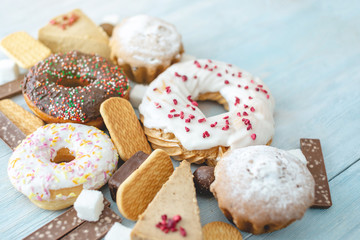 Harmful sweet foods on blue wooden background. Donuts and muffins on the table pile. Unhealthy diet and overweight