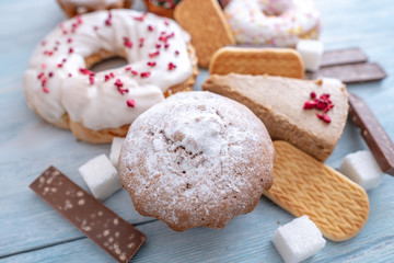 Harmful sweet foods on wooden background. Donuts, muffins, chocolates on the table pile. Unhealthy diet and overweight