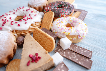 Harmful sweet foods on wooden background. Donuts, muffins, chocolates on the table pile. Unhealthy diet and overweight