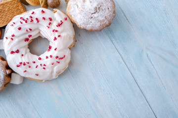 Harmful sweet foods on blue wooden background. Donuts and muffins on the table pile. Unhealthy diet and overweight