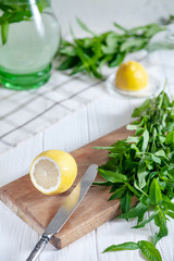 Preparation of the lemonade drink. Cutted lemon on board with fresh mint. Refreshing, cold, summer drink. Lemonade pitcher. Making traditional, healthy lemonade. Ingredients for making mojito