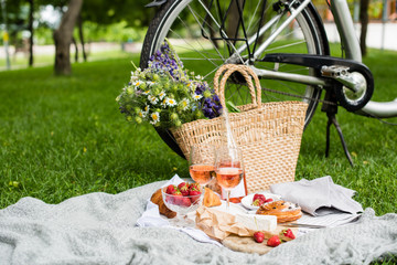 Beautiful summer picnic with strawberries, cheese and rose wine on the lawn in the city park