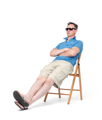 Happy man in shorts, t-shirt, sunglasses is resting on a chair on the beach, isolated on white background