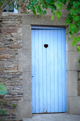 Vintage blue wooden toilet door in an outside stone built old building covered with plants