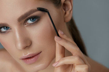 Eyebrow makeup. Woman brushing brows with gel brush closeup