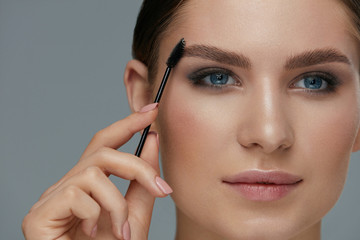 Eyebrow makeup. Woman brushing brows with gel brush closeup