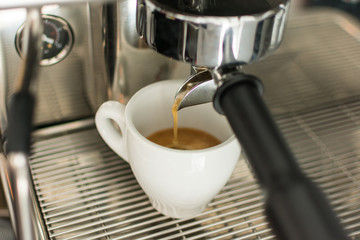 Espresso pouring from coffee machine into one cup