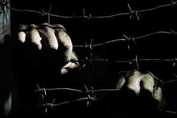 Dirty male hands hold stretched rusty barbed wire in the dark