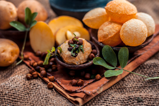 Famous Indian & Asian street food dish i.e. Golgappa snack in a clay bowl along with its flavored spicy water in another clay vessel. Horizontal shot of the snack and its ingredients present.