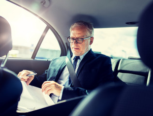transport, business trip, paperwork and people concept - senior businessman with documents and pen driving on car back seat