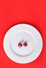 Cherries pair on a white plate isolated on a red background viewed from above. Top view. Copy space. Minimal diet concept