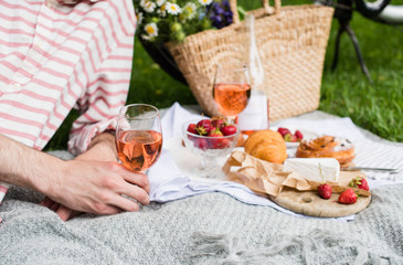 Man's hand holding glass of rose wine, summer picnic with cheese and wine
