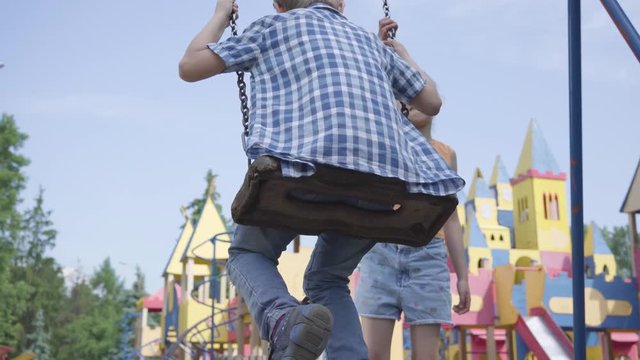 Cute girl with long hair swinging on a swing cute boy outdoors. Couple of happy children. Funny carefree kids in love.