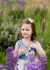 Portrait of little girl in flowers. Cute smiling kid in Blooming Lupine flowers field. Lupinus polyphyllus field