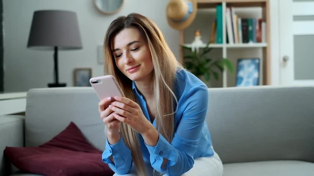 Girl using mobile device browsing the internet, staying connected at home enjoying modern lifestyle. Pretty young woman using smartphone on the couch, texting while relaxing.