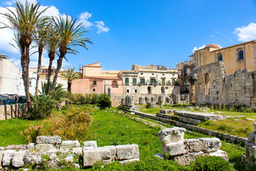 Fototapeta na wymiar Amazing ruins of Temple of Apollo in Ortigia Island, Syracuse, Sicily, Italy. Significant ancient Greek monument, archaeological site. Temple ruins. Adjacent palm trees, sunny day, blue sky