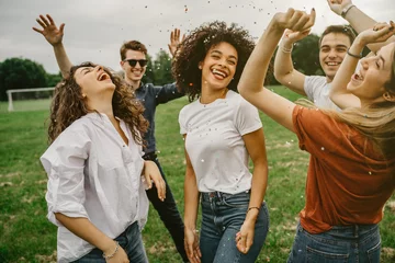 Fotobehang Groep van vijf vrienden die plezier hebben in het park - Millennials dansen in een weiland tussen confetti die in de lucht wordt gegooid - Dag van vrijheid en zorgeloos © loreanto