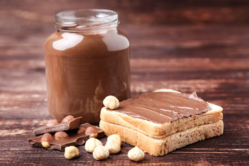 Bread with melted chocolate and glass jar on brown wooden table