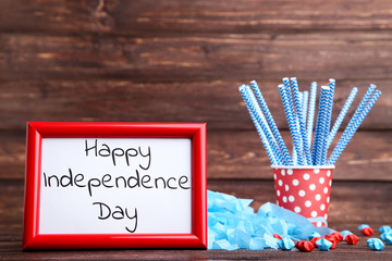 Fototapeta premium Text Happy Independence Day with paper stars and straws in cup on wooden table