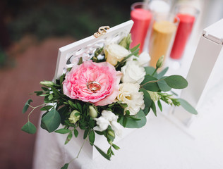 Wedding rings closeup lie on beautiful flowers, a rose and in a modern stylized box on a round white table. Wedding decorations and details. Celebration and ceremony.