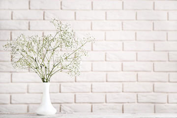 White gypsophila flowers in vase on brick wall background