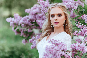 Fototapeta premium Beautiful woman enjoying lilac garden, young woman with flowers in green park. cheerful teenager walking outdoor. soft light style color.