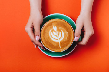 Female hands with a coffee cappuccino cyan cup. Sunny orange toned photo. Warm concept