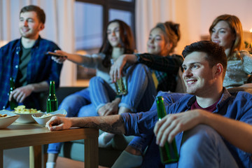 friendship and leisure concept - happy friends with non-alcoholic drinks watching tv at home in evening