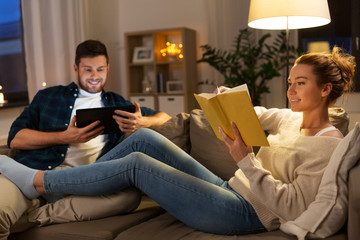 leisure and people concept - happy couple with tablet computer and book at home in evening