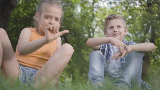 Portrait two funny kids sitting on the grass in the park playing. The boy playing with a bug, girl trying to take it. A couple of happy children. Funny carefree kids rest outdoors. Bottom view