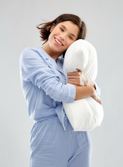 people and bedtime concept - happy young woman in pajama hugging pillow over grey background