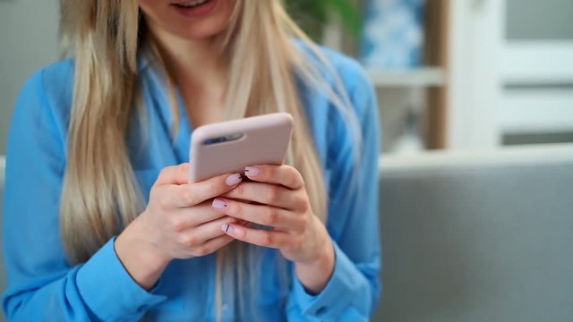 Close up of women's hands holding cell pink telephone, girl texting using app and watching video on mobile phone, enjoying reading social media at home.