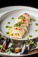 The concept of Italian cuisine. Pasta with cream sauce, pesto and seafood, mussels. European cuisine. Serving dishes in the restaurant with microgreen. copy space